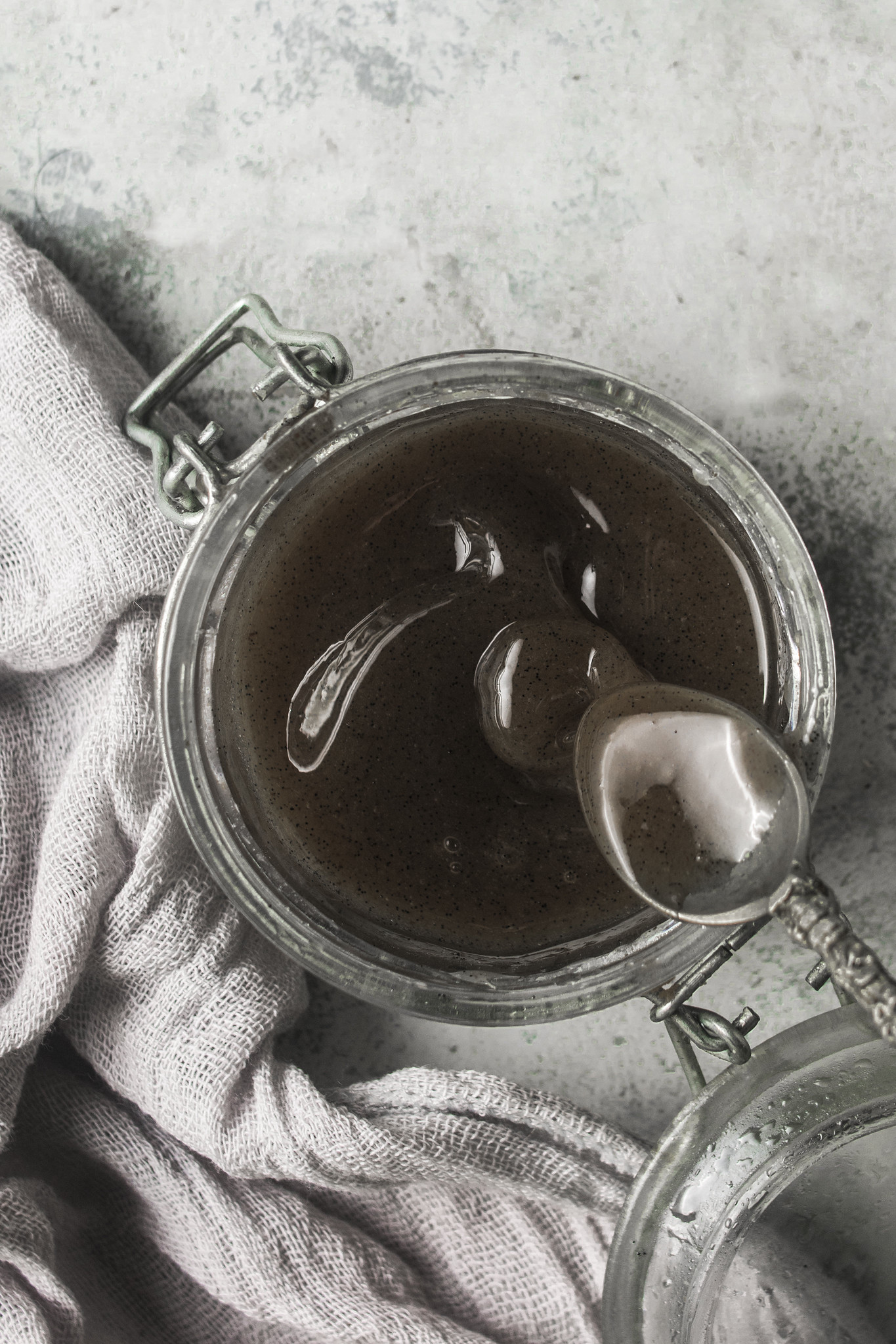 Thick homemade vanilla bean paste slowly falling from a spoon into a jar.